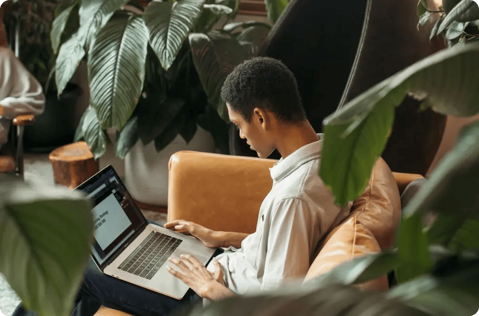 Homme travaillant sur une stratégie éditoriale sur un canapé, entouré de plante.